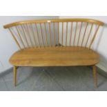 A mid-century blond elm Windsor love seat by Ercol, on canted supports with an ‘H’ stretcher.
