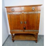 An Arts & Crafts medium oak cabinet featuring ornate pierced steel escutcheons, drop ring handles