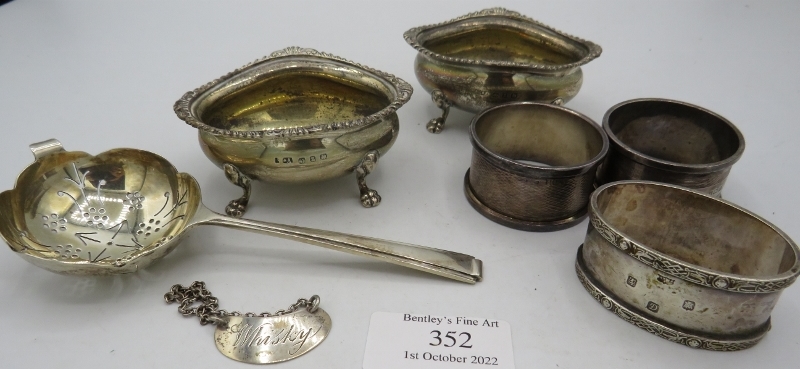 A pair of silver salts with cast lions paw feet. Birmingham 1899, a silver tea strainer, Sheffield