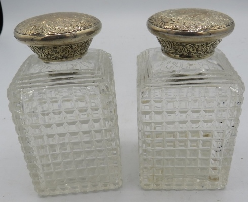 A pair of Victorian square cut glass scent bottles with engraved silver tops, both with inner