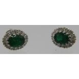 A pair of 18ct white gold oval emerald and round brilliant cut diamond cluster stud earrings.