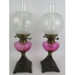 A pair of antique oil lamps with cast iron bases decorated with birds, cranberry glass reservoirs