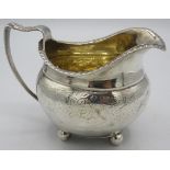 A Georgian silver cream jug with engraved decoration, gilded interior and on ball feet. Hallmarks