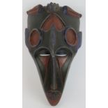 A carved wood West African tribal mask decorated in blue and red polychrome colours. Height 42cm.