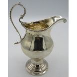 A Georgian silver pedestal cream jug with bead edge decoration & double scroll handle. Floral