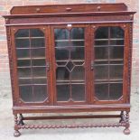 A 1920s Jacobean Revival glazed bookcase featuring carved frieze, the tracery glazed doors opening