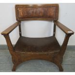 An Arts & Crafts oak ‘X’ frame armchair with embossed leather back best and carved detail to legs.