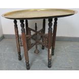 A vintage Benares table, the brass tray top hand tooled with Egyptian motifs, on folding oak