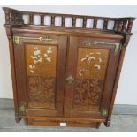 An Arts & Crafts oak wall hanging cabinet with ¾ gallery, featuring ornate brass hinges and inset
