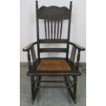 An Edwardian ebonised rocking chair with carved backrest featuring turned spindles and bergère seat,