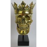 A contemporary polished bronze model of a human skull wearing a crown mounted on a bespoke plinth.