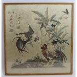 An antique Chinese silk work panel depicting a pair of fighting cockerels with Chinese characters