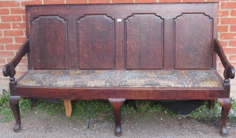 An 18th century oak settle, the backrest with fielded panels, joined with open-sided armrests, on