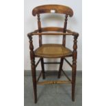 An Edwardian oak child’s highchair with bergère seat, on turned supports with stretchers.