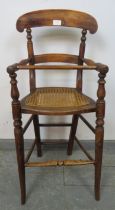 An Edwardian oak child’s highchair with bergère seat, on turned supports with stretchers.