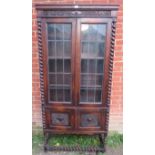 A tall 1920s Jacobean Revival oak bookcase featuring barley twist uprights, the glazed doors with