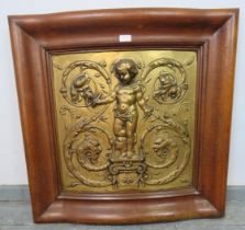 A Rococo embossed gilt brass panel depicting a cherub holding compasses and quill, mounted in an oak