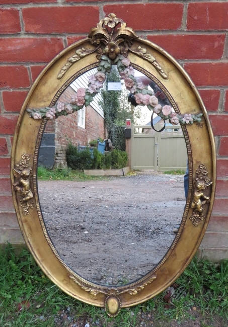 A 19th century oval wall mirror in an ornate gilt gesso frame featuring polychrome decoration in the