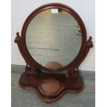 A Victorian mahogany oval swing vanity mirror, with scrolled and pierced uprights, on a shaped