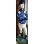 A life-size painted plaster figure of a jockey in racing colours, with riding crop, on a plinth