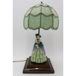 An early to mid-20th century table lamp, the polished wood base mounted with a porcelain figure of a