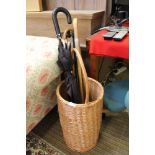 Woven wicker cylindrical stick stand with fixed handle containing a small selection of sticks and