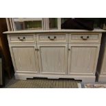 A lime wash effect side unit with three in line drawers over three plane panelled cupboard doors