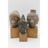 A collection of three Buddha heads, one bronze, the other two terracotta, raised on wooden plinth