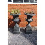 A pair of cast iron campagna form garden urns on plinth base, grey painted.