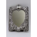 An embossed silver mounted dressing table mirror, flowers & putti repousse frame forming a heart