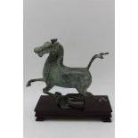 In the Classical style, a patinated bronze galloping horse statuette, raised upon a stained wood