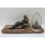 A French Art Deco table lamp, a gilded spelter young woman reclining on a marble base, beside a