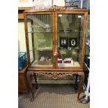 A reproduction walnut coloured display cabinet on four-legged stand
