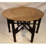 An early 20th century Indian brass tray top table, on carved wood folding frame, the top engraved to