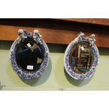 A pair of oval bevel plate wall mirrors, in floral porcelain frames surmounted by twin putto