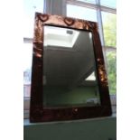 An Arts & Crafts copper framed rectangular bevel plate wall mirror, with a trio of heart motifs