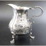 A George II silver cream jug, repousse floral decoration, scroll handle, raised on three trefoil sup