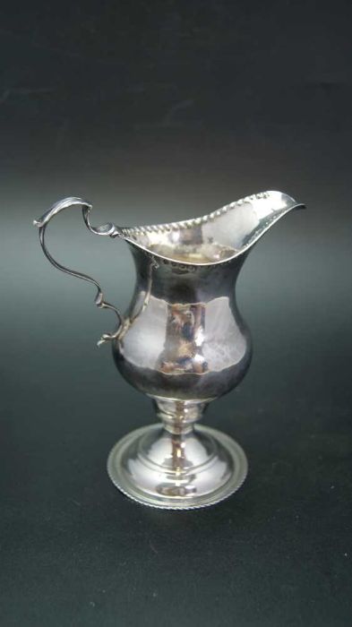 A George III silver cream jug of baluster form with punched rim, C scroll handle and raised circular - Image 2 of 5