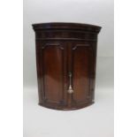 A George III oak bow front hanging corner cupboard, with dentil cornice and mahogany inlay,