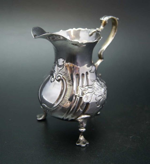 John Muns, a George III silver cream jug, embossed floral decoration, raised on three trefid support