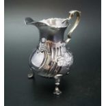 John Muns, a George III silver cream jug, embossed floral decoration, raised on three trefid support