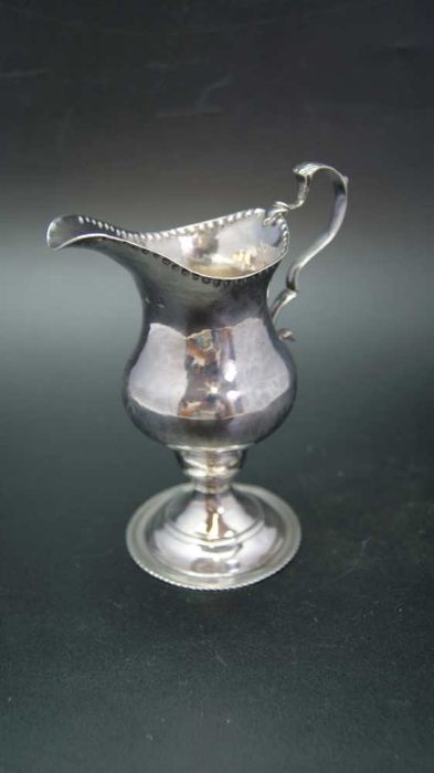 A George III silver cream jug of baluster form with punched rim, C scroll handle and raised circular