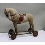 An early 20th century push-along upholstered horse, with saddle on metal frame base, with rubber tyr