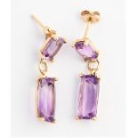 A pair of amethyst drop stud earrings, each set with an elongated cushion cut amethyst suspended