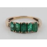 A hallmarked 9ct yellow gold emerald and diamond ring, set with five graduated emerald-cut emeralds,