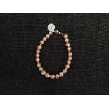 A peach cultured pearl bracelet, with gold-tone spacers, clasp stamped 375, length approx. 7½".