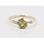 A hallmarked 9ct yellow gold peridot and colourless stone ring, set with a pear cut peridot, flanked