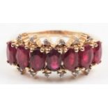 A hallmarked 9ct yellow gold ruby and colourless stone half eternity ring, set with seven oval cut