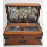 An oak tantalus, to include three decanters and four cups in foldaway drawer, with key included.