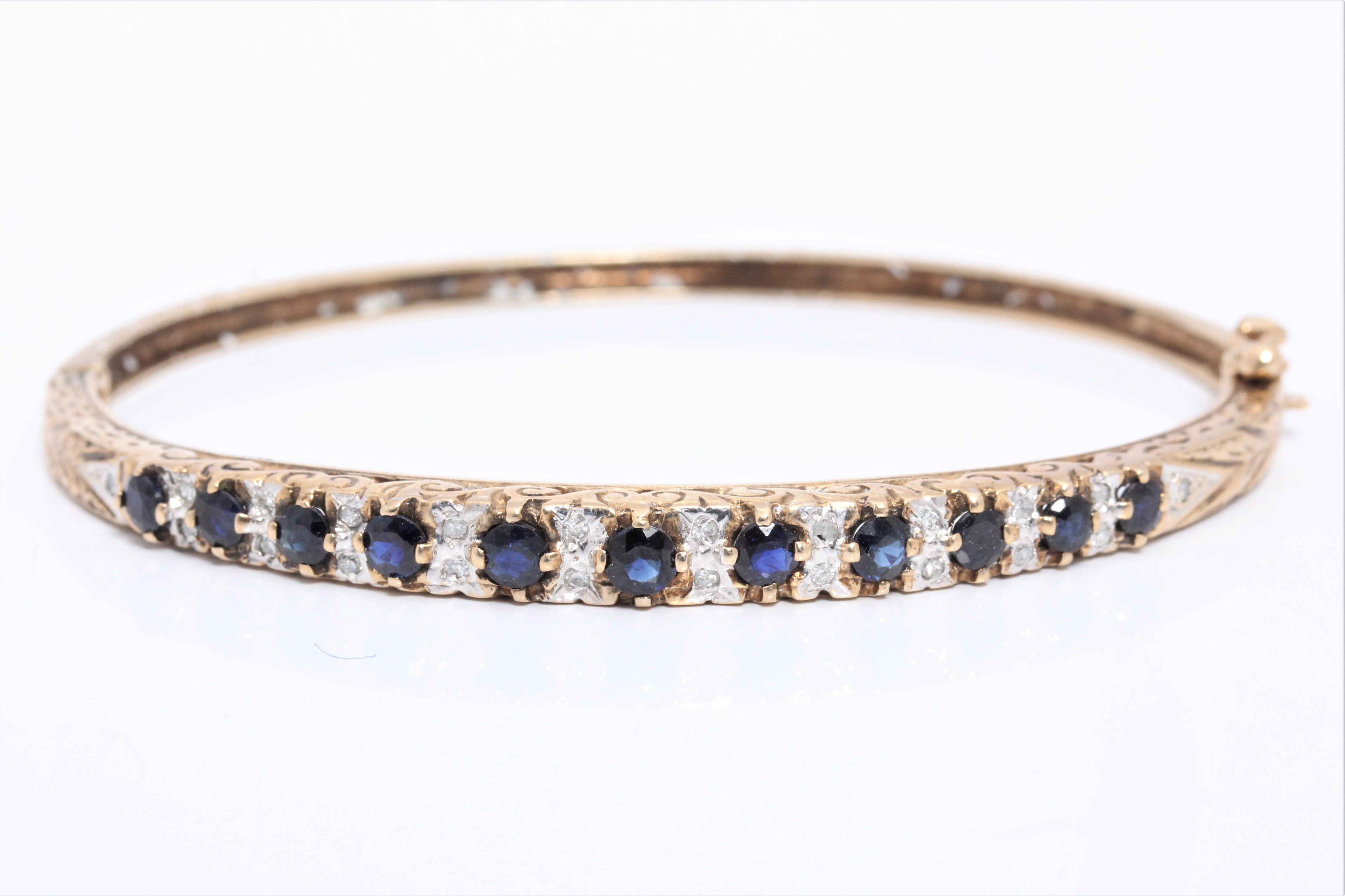 A hallmarked 9ct yellow gold sapphire and diamond hinged bangle, set with eleven graduated round cut